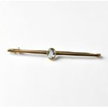A yellow metal bar brooch with an oval bezel set blue stone, possibly aquamarine, length 6cm,