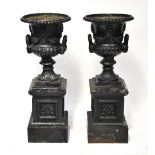 A pair of black painted cast iron twin-handled urns on square section base,