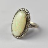 An opal and diamond ring with large white claw set opal within a border of tiny diamonds,