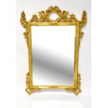 A gilt framed wall mirror with rectangular plate surrounded by pierced Rococo-style C-scrolls,