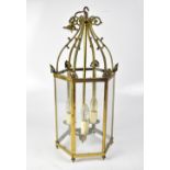 A hexagonal brass-effect lantern-style ceiling light with three candle-effect lights below a