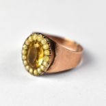 A rose gold ring with central oval citrine-coloured stone surrounded by a border of small seed