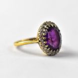 An 18ct gold dress ring with central cut claw set oval amethyst within a border of tiny diamonds,