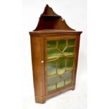 A mahogany floor standing corner cupboard with shaped upper shelf above astragal glazed door,