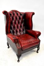 A contemporary oxblood leather button pressed wing backed armchair,