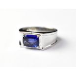 An 18ct white gold gentlemen's ring set with a central sapphire in a four-claw enclosed setting,