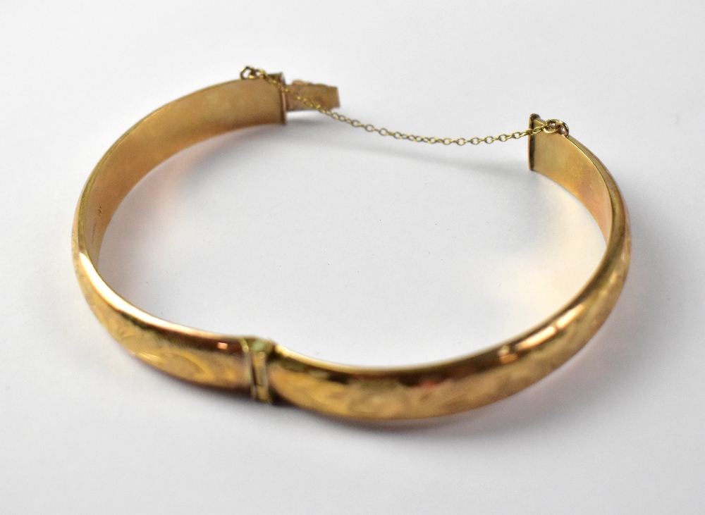 A 9ct yellow gold bangle with chased scroll decoration and safety chain, approx 11.5g.