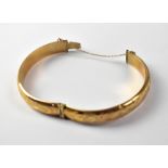 A 9ct yellow gold bangle with chased scroll decoration and safety chain, approx 11.5g.