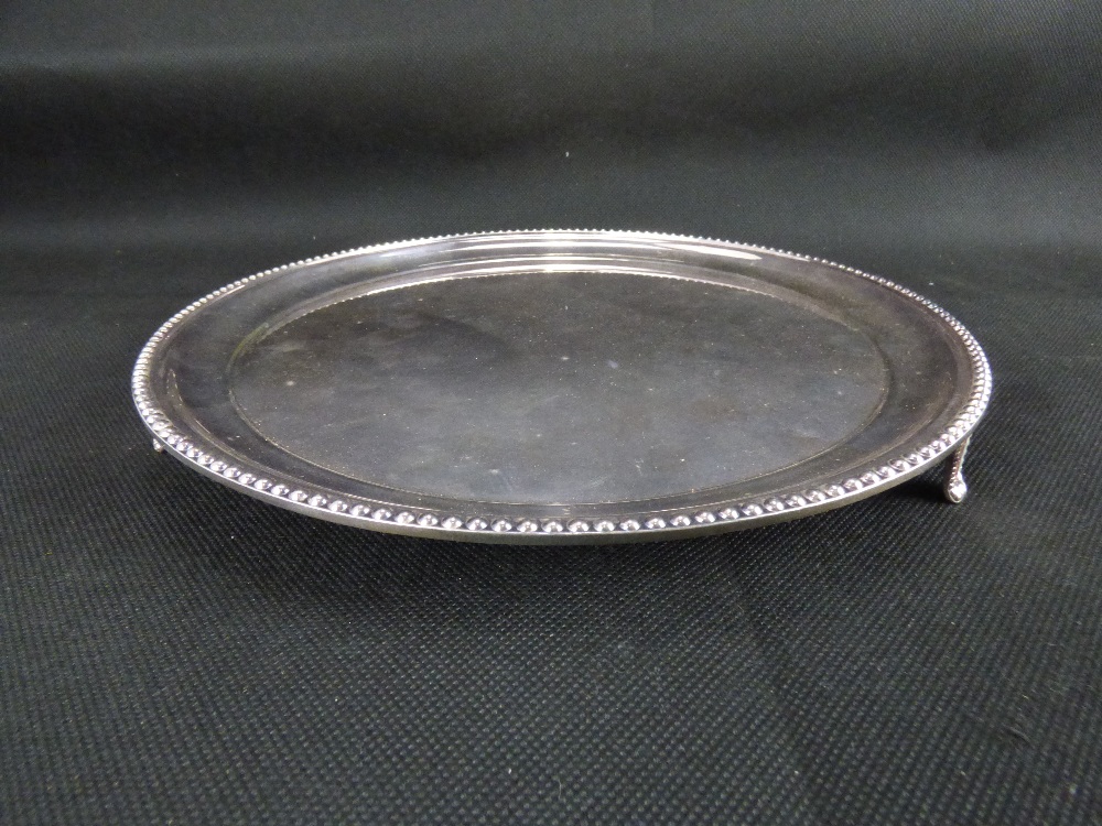 A modern hallmarked silver circular tray with beaded edge, raised on three triangular feet,