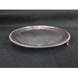 A modern hallmarked silver circular tray with beaded edge, raised on three triangular feet,