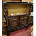 A dark oak side cabinet, the hinged upper door flanked by applied carved figural mounts,