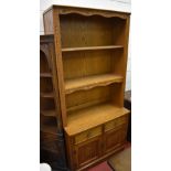 An oak side cabinet with adjustable upper shelf above a fixed shelf with shaped apron and base of