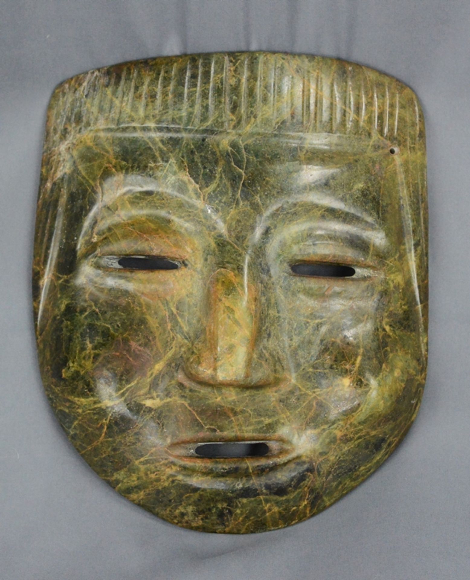 Steinmaske, in Form eines menschlichen Kopfes, flache Nase, und eine deutlich erhobene Wange, Schli