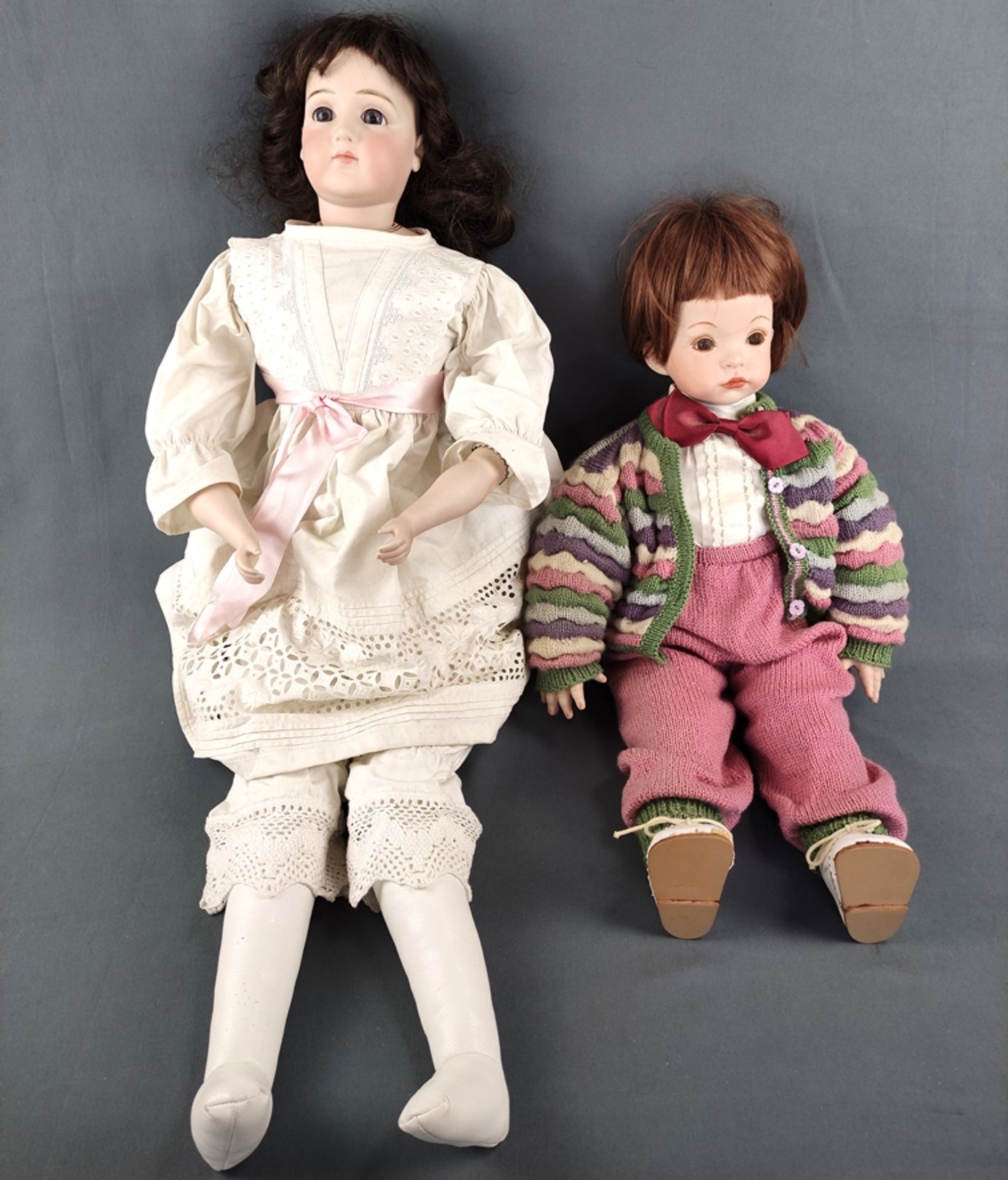 Two dolls, one with blue glass eyes, closed mouth and brown curly wig, head and hands made of bisqu