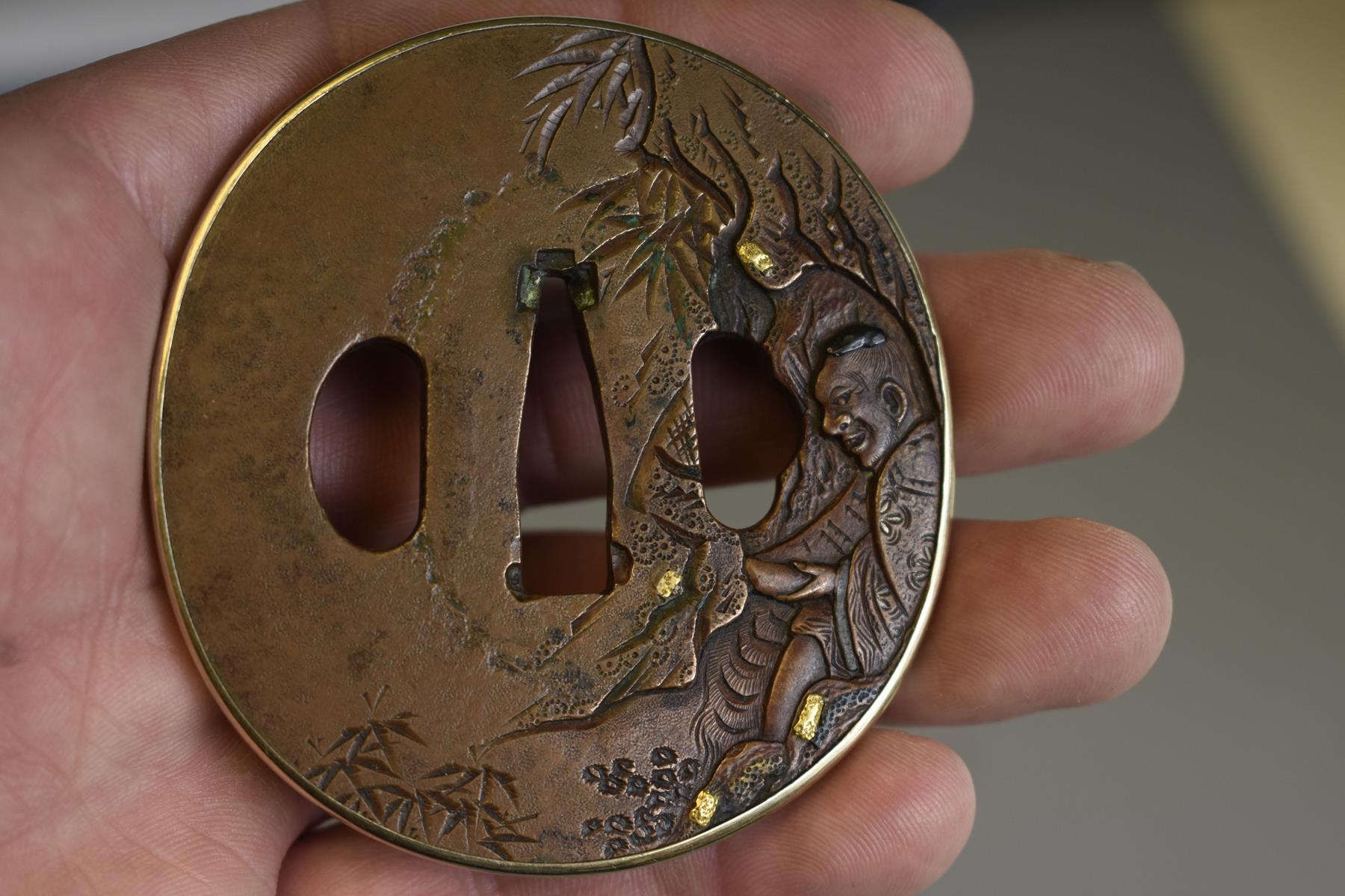 A CIRCULAR COPPER TSUBA, decorated with a figure in a cave within a landscape, gold and shakudo - Image 3 of 5