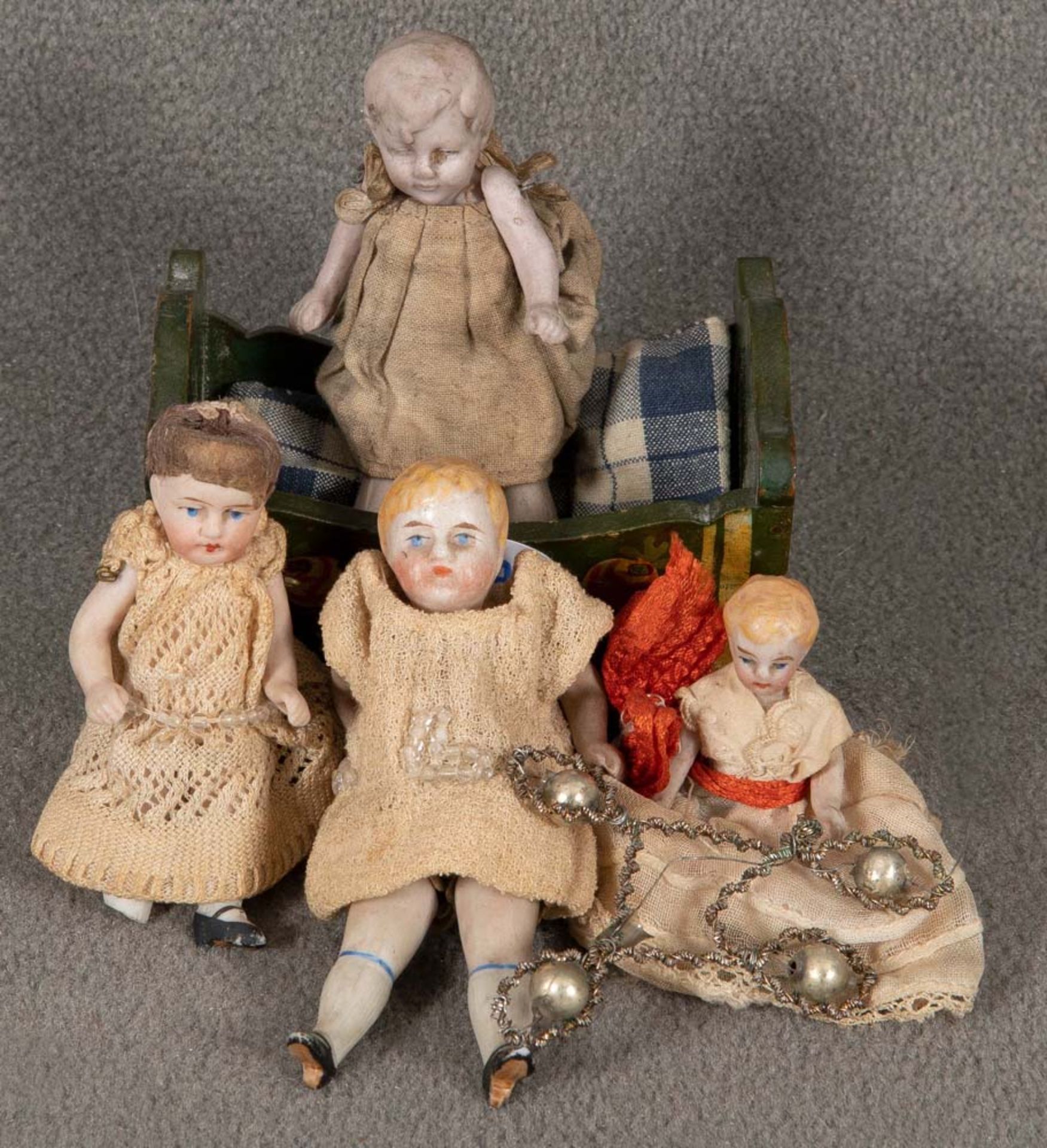 Vier kleine Puppen. Deutsch um 1900. Porzellan, mit Kleidern; dazu eine Wiege.
