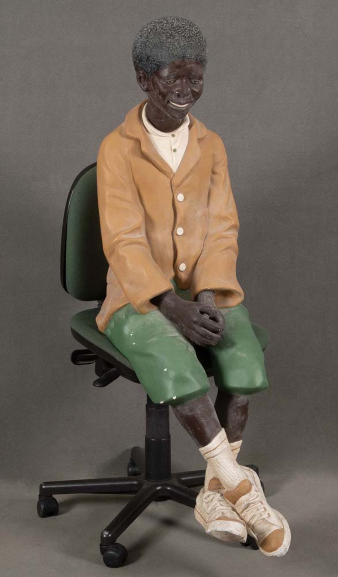 Sitzender dunkelhäutiger Junge. Wohl England 20. Jh. Gips, bemalt, H=130 cm. (ohne Stuhl), (