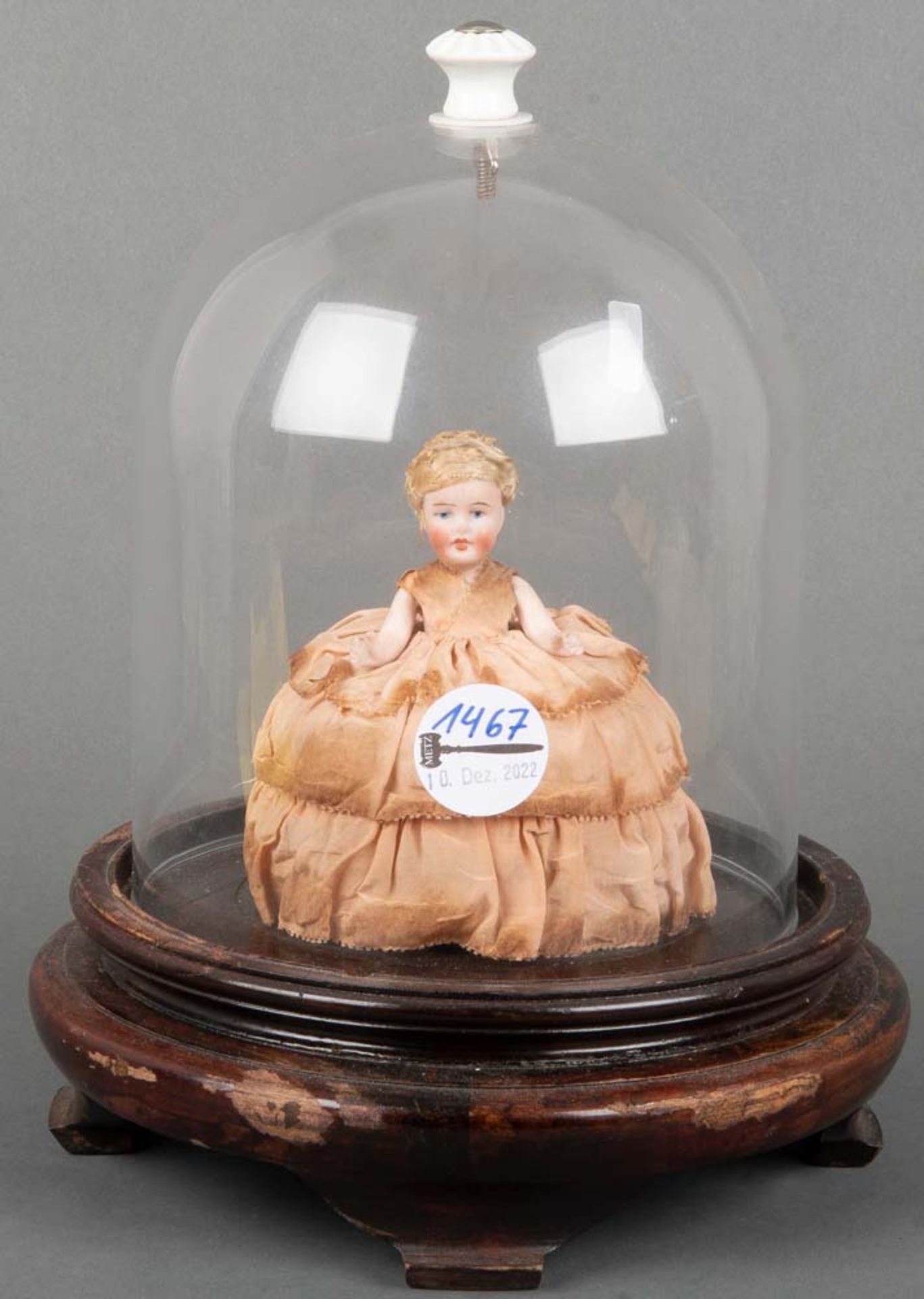Kleine Puppe. Wohl Deutsch um 1900. Porzellan, Stoffkleid; unter Glassturz auf Holzsockel, H=12 bzw.