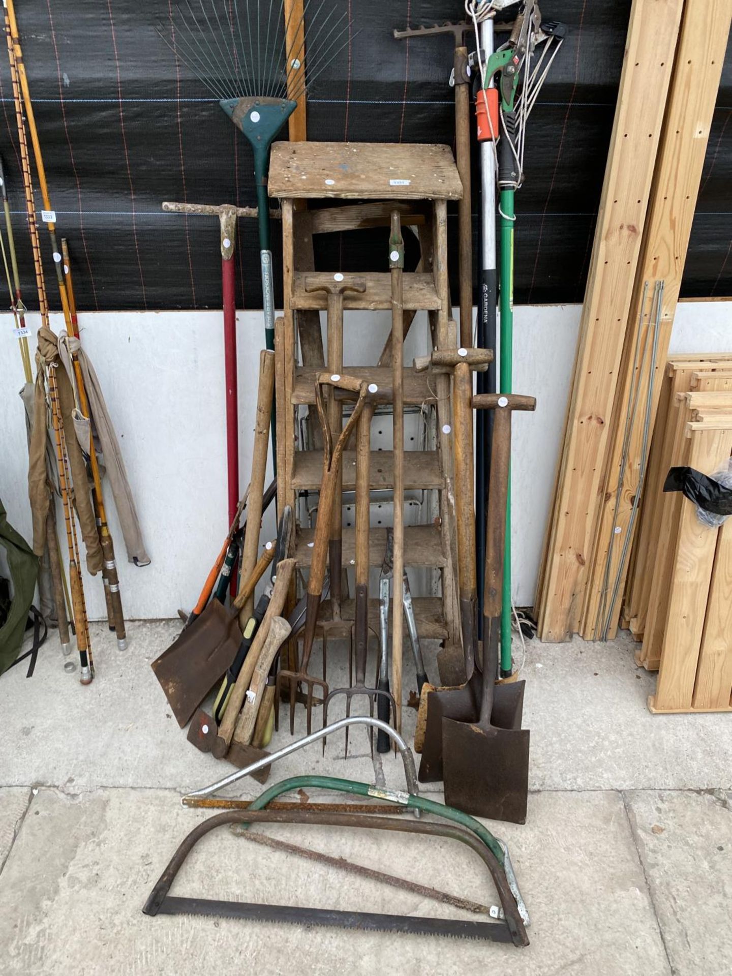 AN ASSORTMENT OF VINTAGE TOOLS TO INCLUDE A WOODEN STEP LADDER, FORKS AND SHOVELS ETC