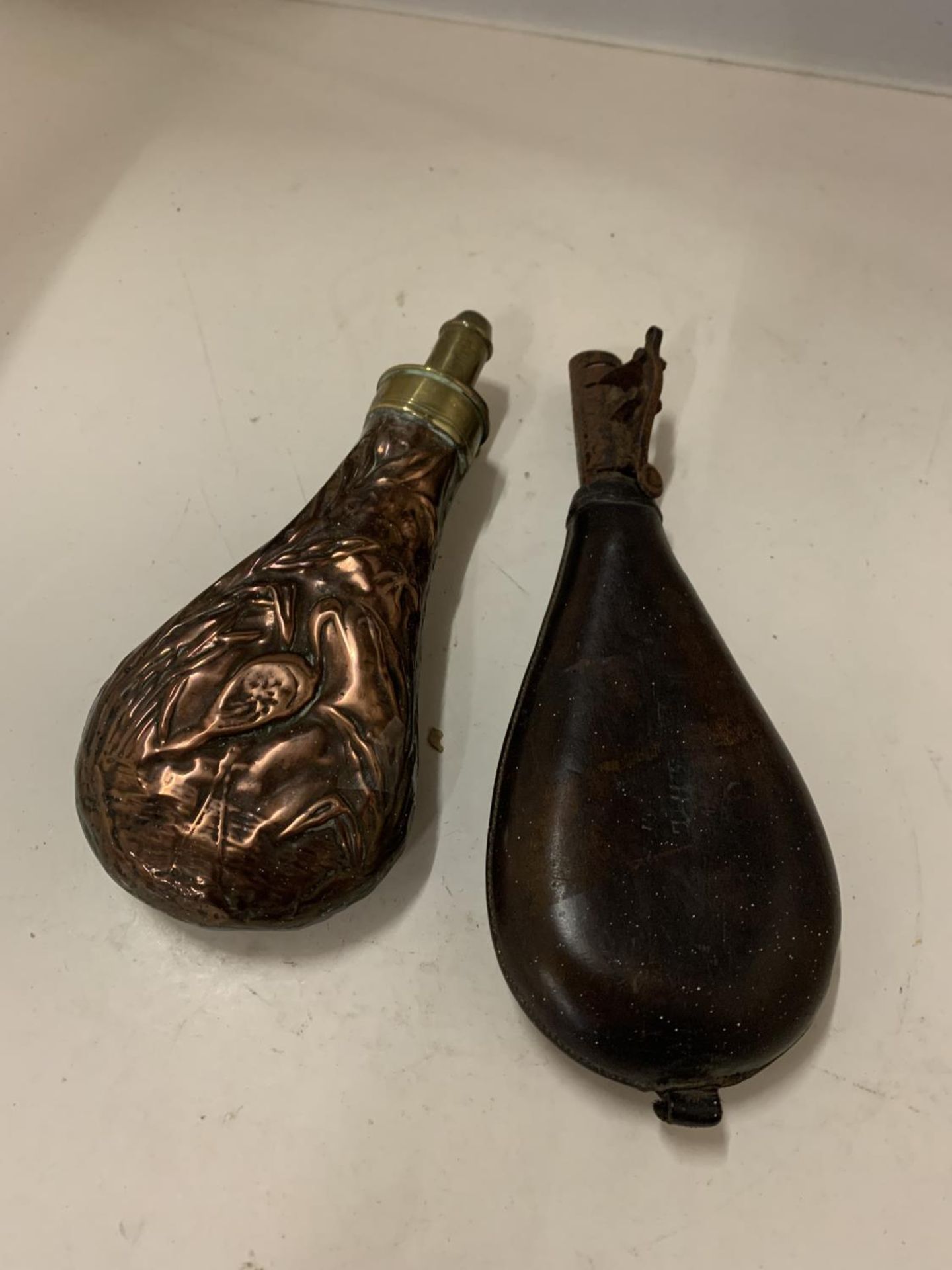 TWO POWDER FLASKS, ONE COPPER AND BRASS AND FURTHER LEATHER AND METAL EXAMPLE