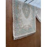 A GREEN AND CREAM PATTERNED FRINGED RUG