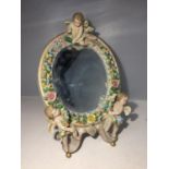 AN OVAL CERAMIC BEVELLED MIRROR DECORATED WITH CHERUBS AND FLOWERS, HEIGHT 30CM