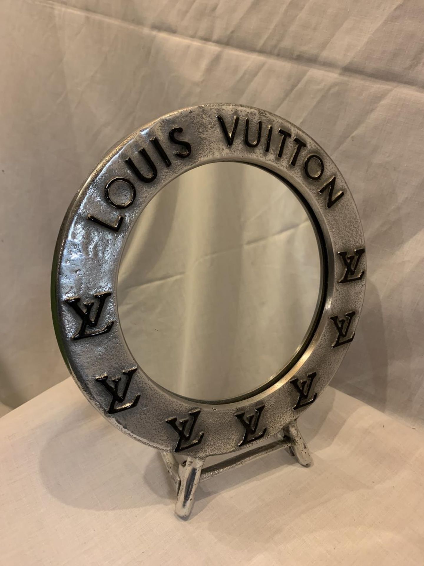 A CHROME LOUIS VUITTON STYLE CIRCULAR MIRROR ON A STAND