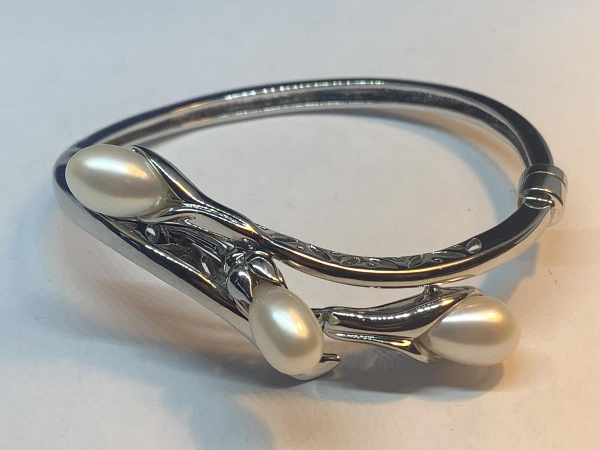 A MARKED 925 SILVER BANGLE WITH THREE PEARLS IN A LILY DESIGN GROSS WEIGHT 23.9 GRAMS WITH A