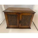 AN EDWARDIAN OAK SMOKERS COMPENDIUM WITH RELIEF CARVED DOORS