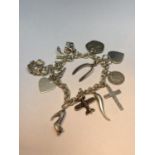 A MARKED SILVER CHARM BRACELET WITH TWELVE VARIOUS CHARMS TO INCLUDE SHOES, PLANES, SHIPS, CROSS,