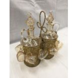 AN ANTIQUE LIQUER DECANTER SET WITH TWO DECANTERS AND TEN CUPS IN A BRASS CARRIER