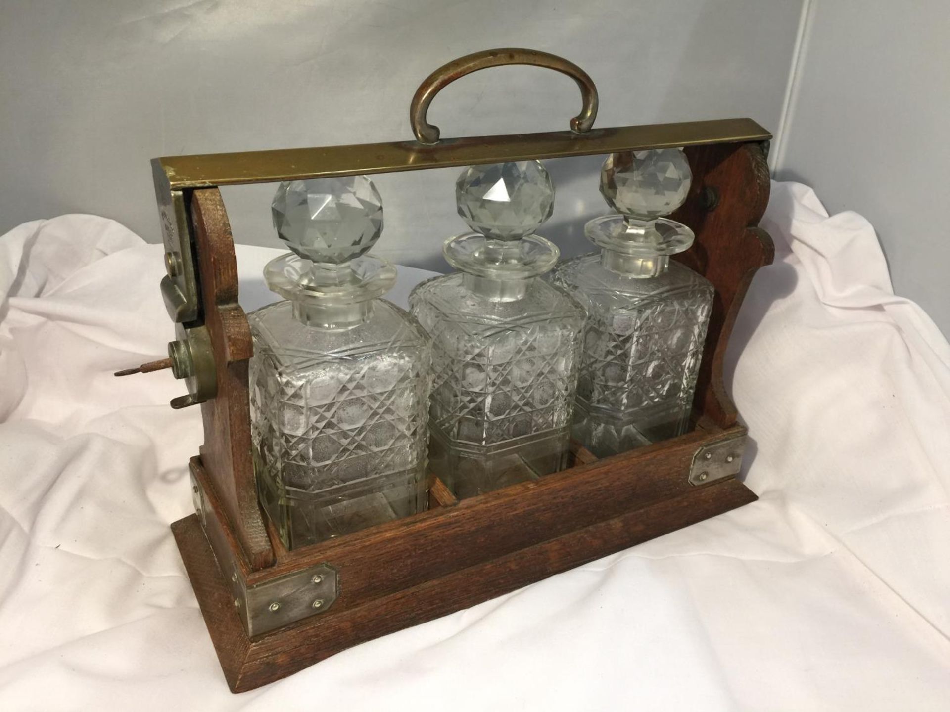 A BETJEMANN LONDON PATENT 62082 OAK FRAMED AND BRASS TANTALUS WITH THREE DECANTERS AND A KEY