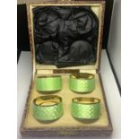 A BOXED SET OF FOUR HALLMARKED BIRMINGHAM NAPKIN RINGS WITH GREEN ENAMEL DECORATION