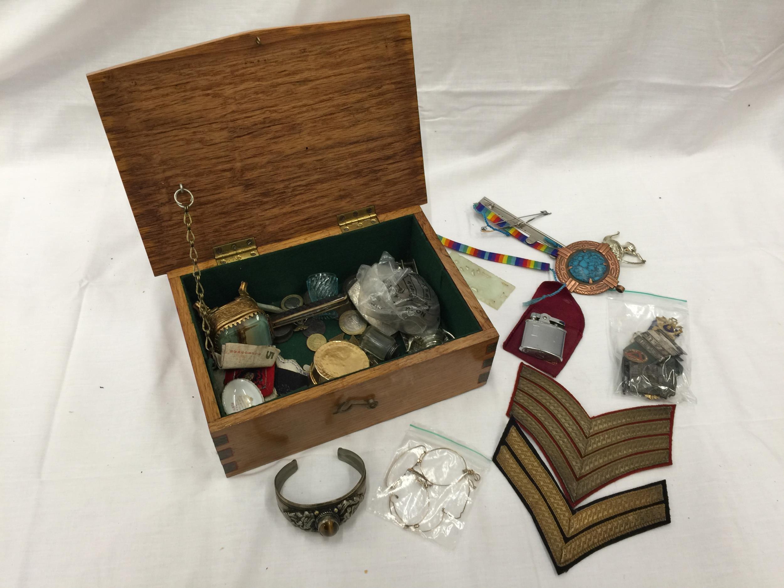 AN OAK BOX WITH A MILITARY EMBLEM CONTAINING MEDALS, BADGES, COINS, PEN KNIFE, LIGHTERS, ETC