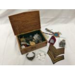 AN OAK BOX WITH A MILITARY EMBLEM CONTAINING MEDALS, BADGES, COINS, PEN KNIFE, LIGHTERS, ETC