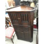 AN OAK JACOBEAN STYLE CORNER CUPBOARD WITH PILLARED GLASS DOORS AND ARCHED PANEL DOORS, 29" WIDE