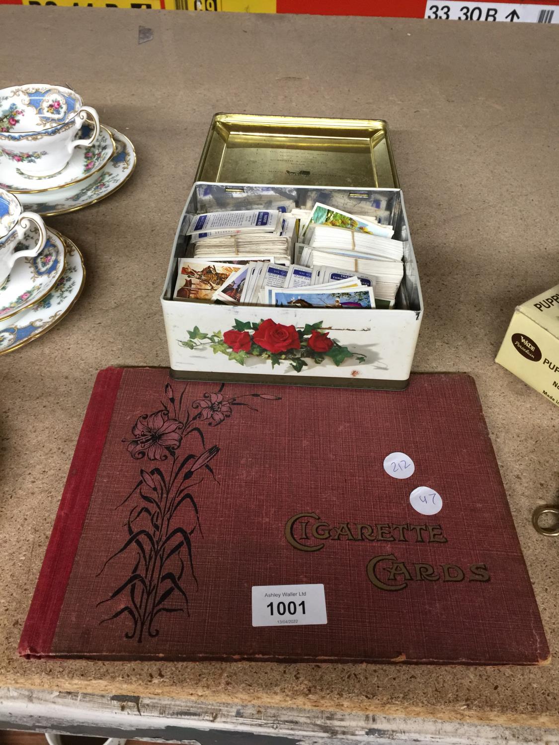 A CIGARETTE CARD ALBUM (EMPTY) AND A TIN CONTAINING CIGARETTE CARDS