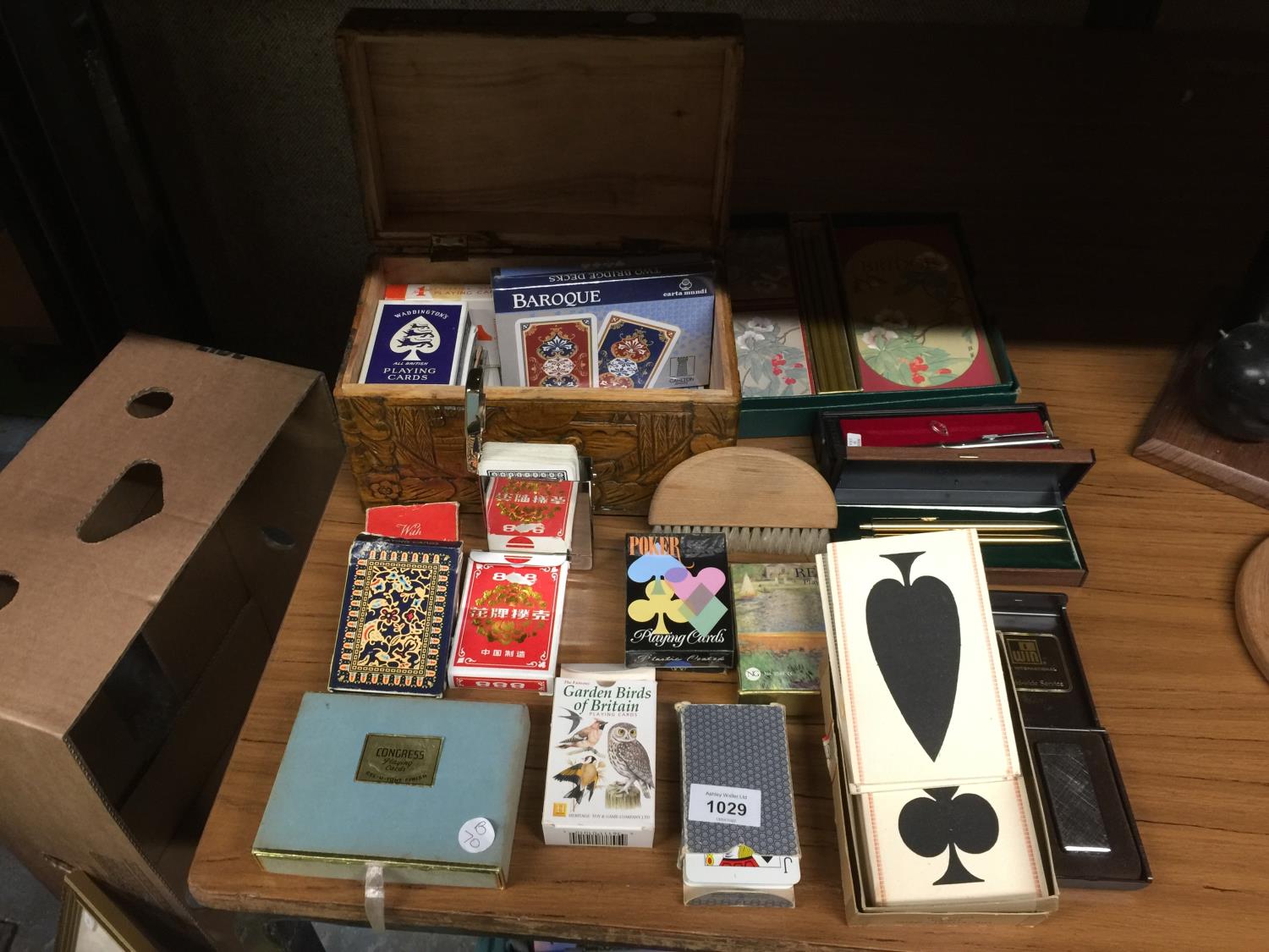 A CARVED WOODEN BOX CONTAINING A QUANTITY OF PLAYING CARDS INCLUDING BAROQUE, PLUS PENS, A LIGHTER