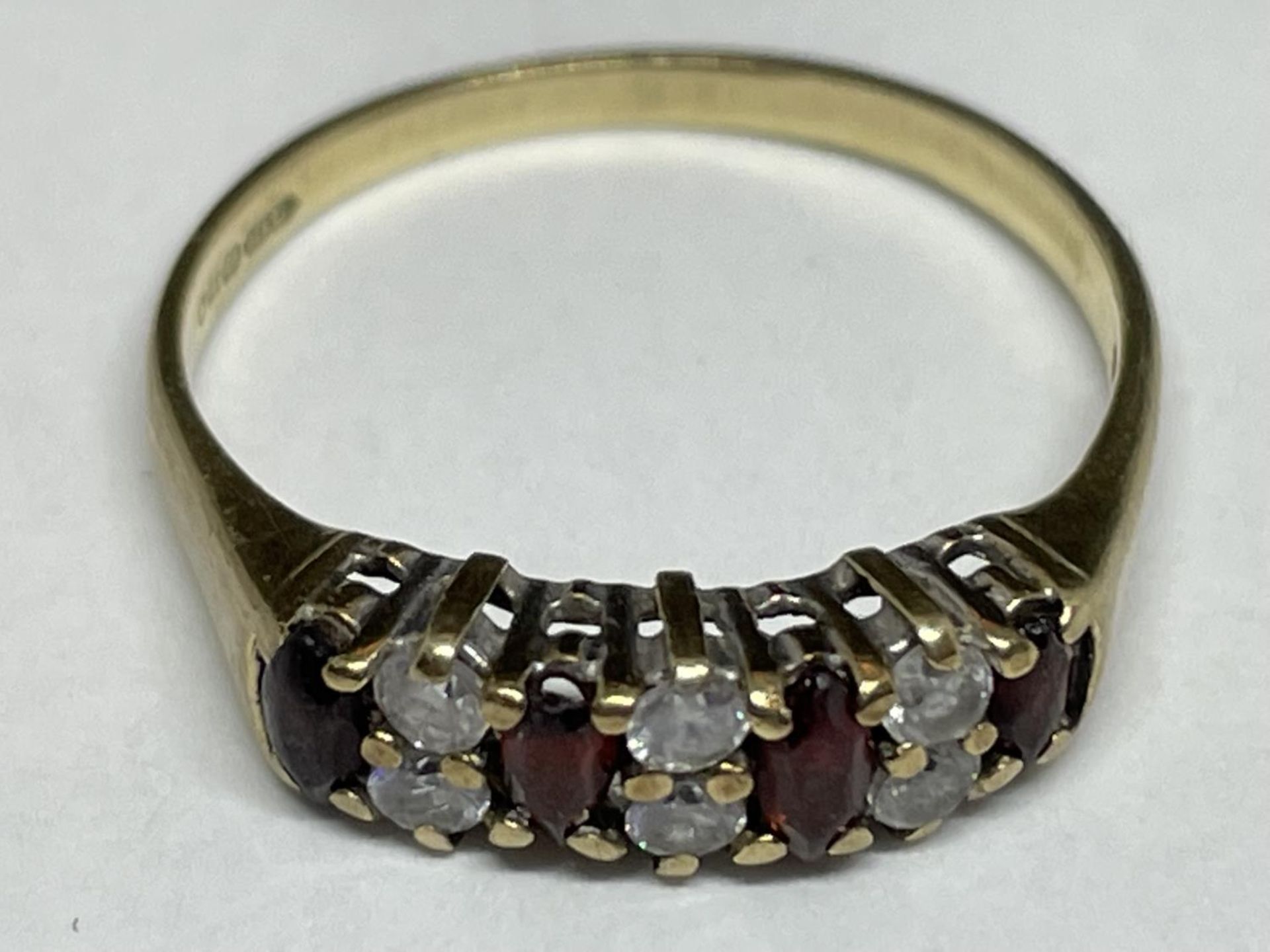 A 9 CARAT GOLD RING WITH FOUR RED STONES AND SIX CLEAR STONES IN A BAND SIZE M