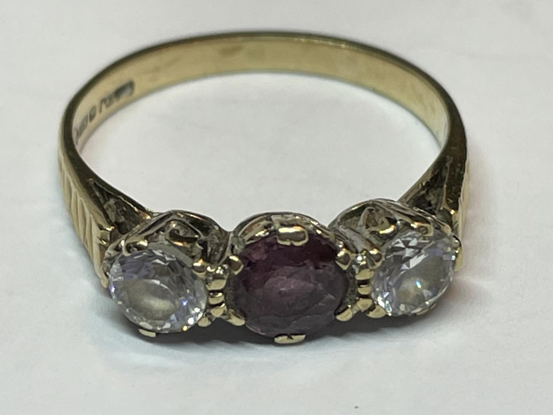 A 9 CARAT GOLD RING WITH AN AMETHYST AND TWO CLEAR STONES IN LINE SIZE K/L