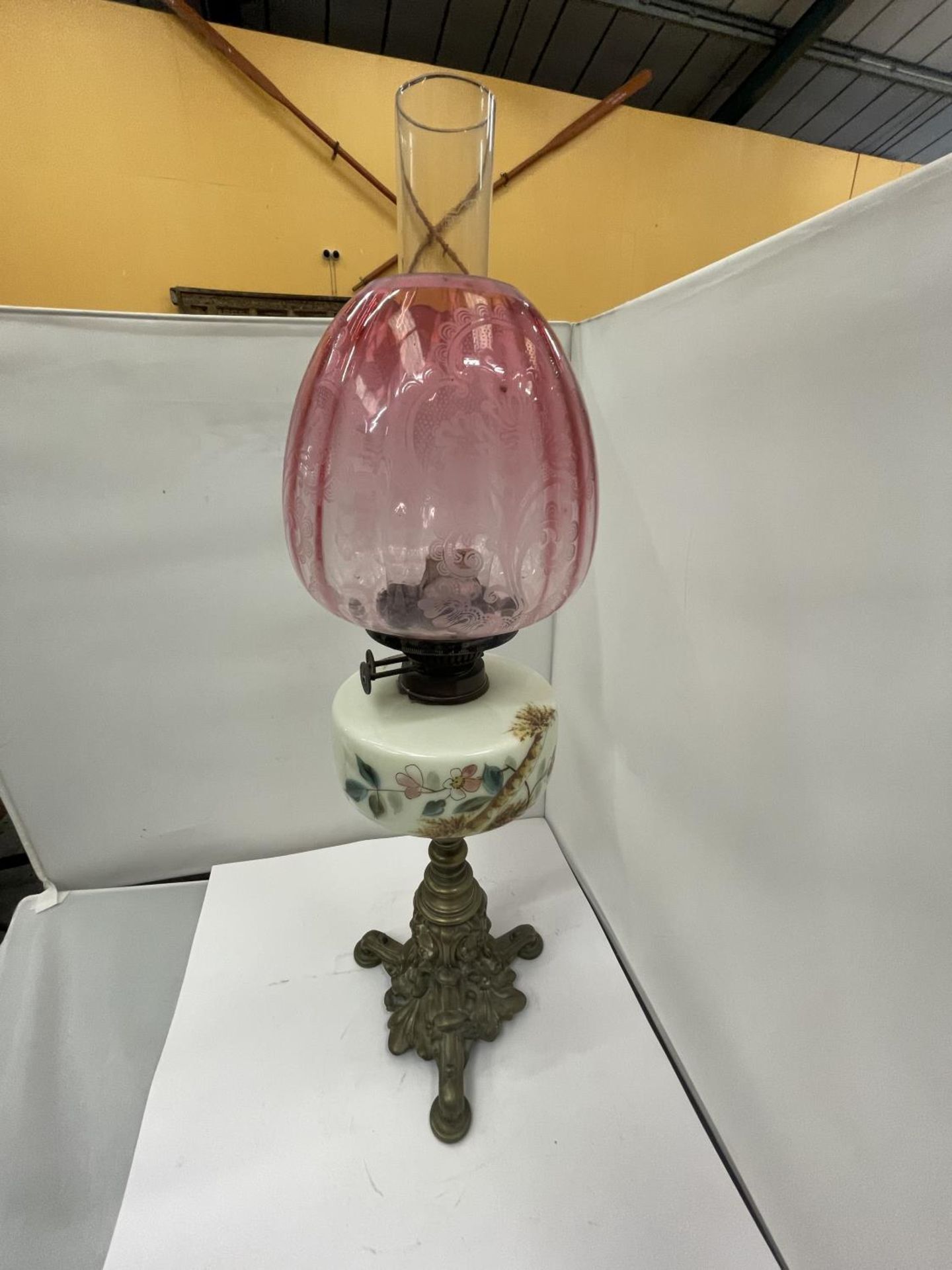 A BRASS OIL LAMP WITH DECORATIVE RESRVOIR, GLASS FUNNEL AND CRANBERRY GLASS SHADE