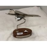 A CHROME REPLICA OF CONCORDE ON A WOODEN STAND 19CM X 21CM