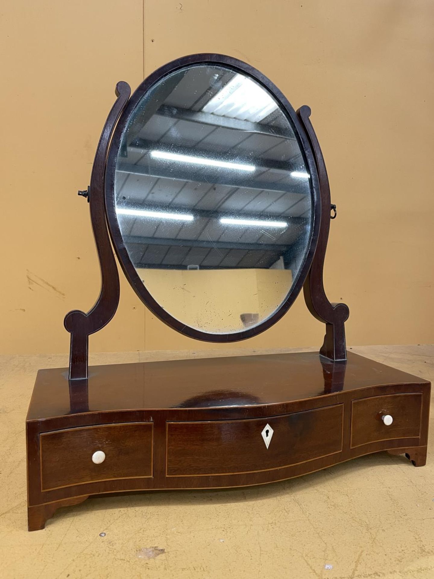A MAHOGANY OVAL DRESSING TABLE MIRROR WITH A SERPENTINE BOW FRONT CONTAINING ONE LONG AND TWO
