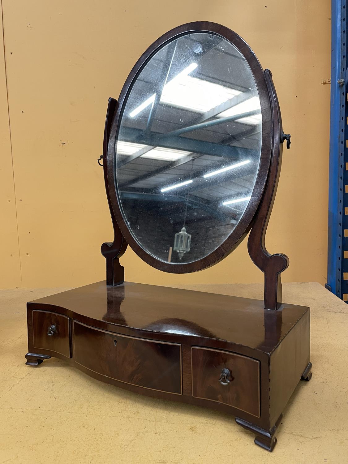 A MAHOGANY OVAL DRESSING TABLE MIRROR WITH A SERPENTINE BOW FRONT CONTAINING ONE LONG AND TWO