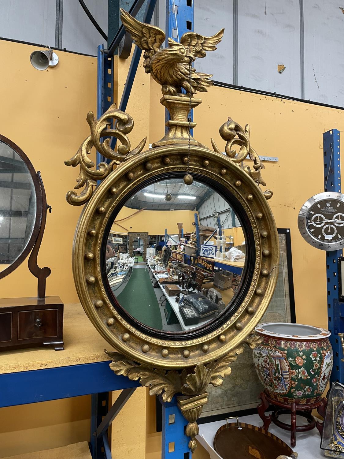 A CIRCULAR REGENCY GILT CONVEX WALL MIRROR 60CM DIAMETER WITH FOLIATE DECORATION TO RIM SURMOUNTED