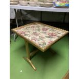 A GILT COLOURED TABLE WITH A FLORAL TAPESTRY TOP THAT FOLDS INTO A FIRE SCREEN