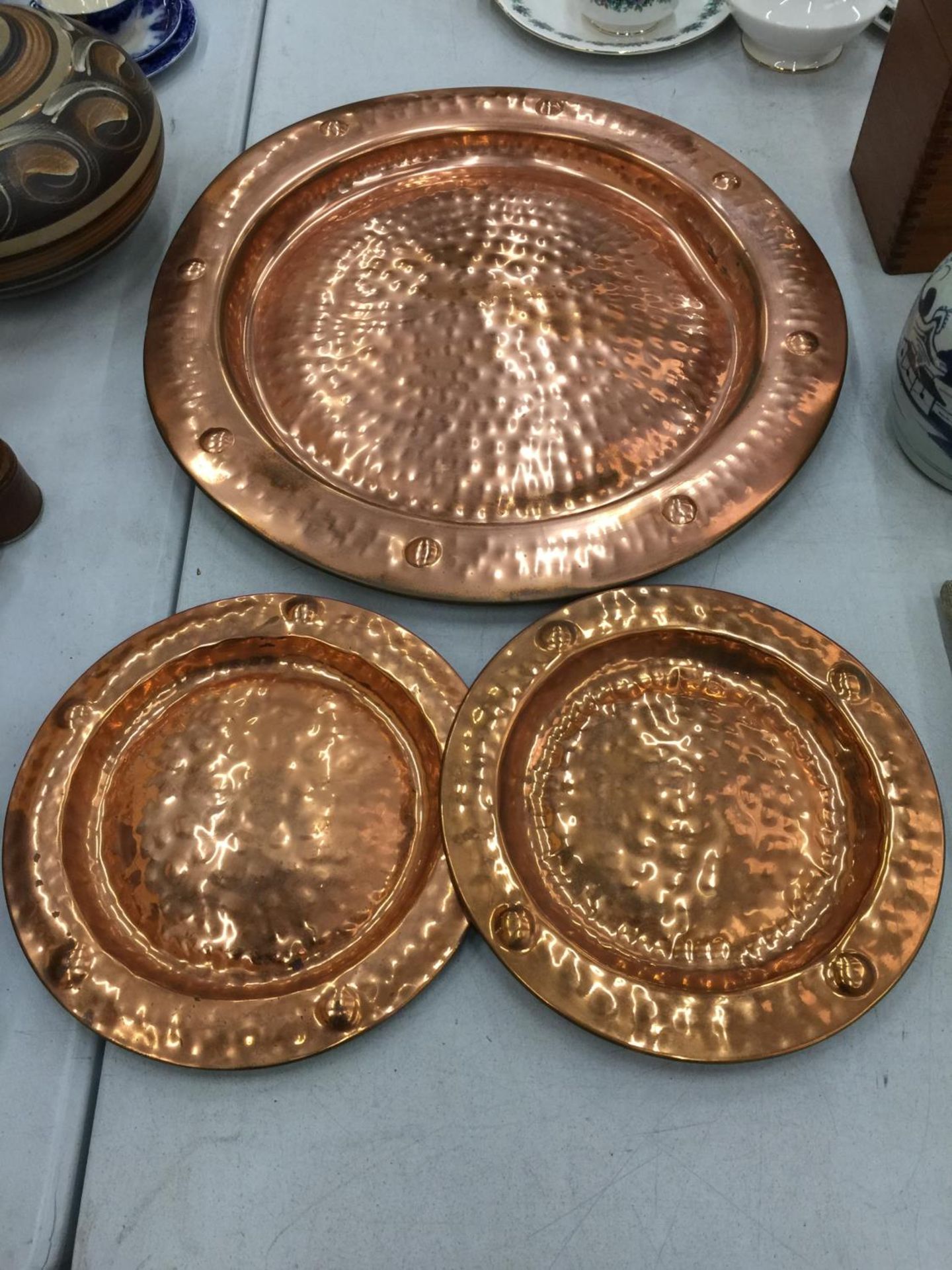 A LARGE AND TWO SMALLER HAND HAMMERED COPPER CHARGERS DIAMETERS 53CM AND 29CM