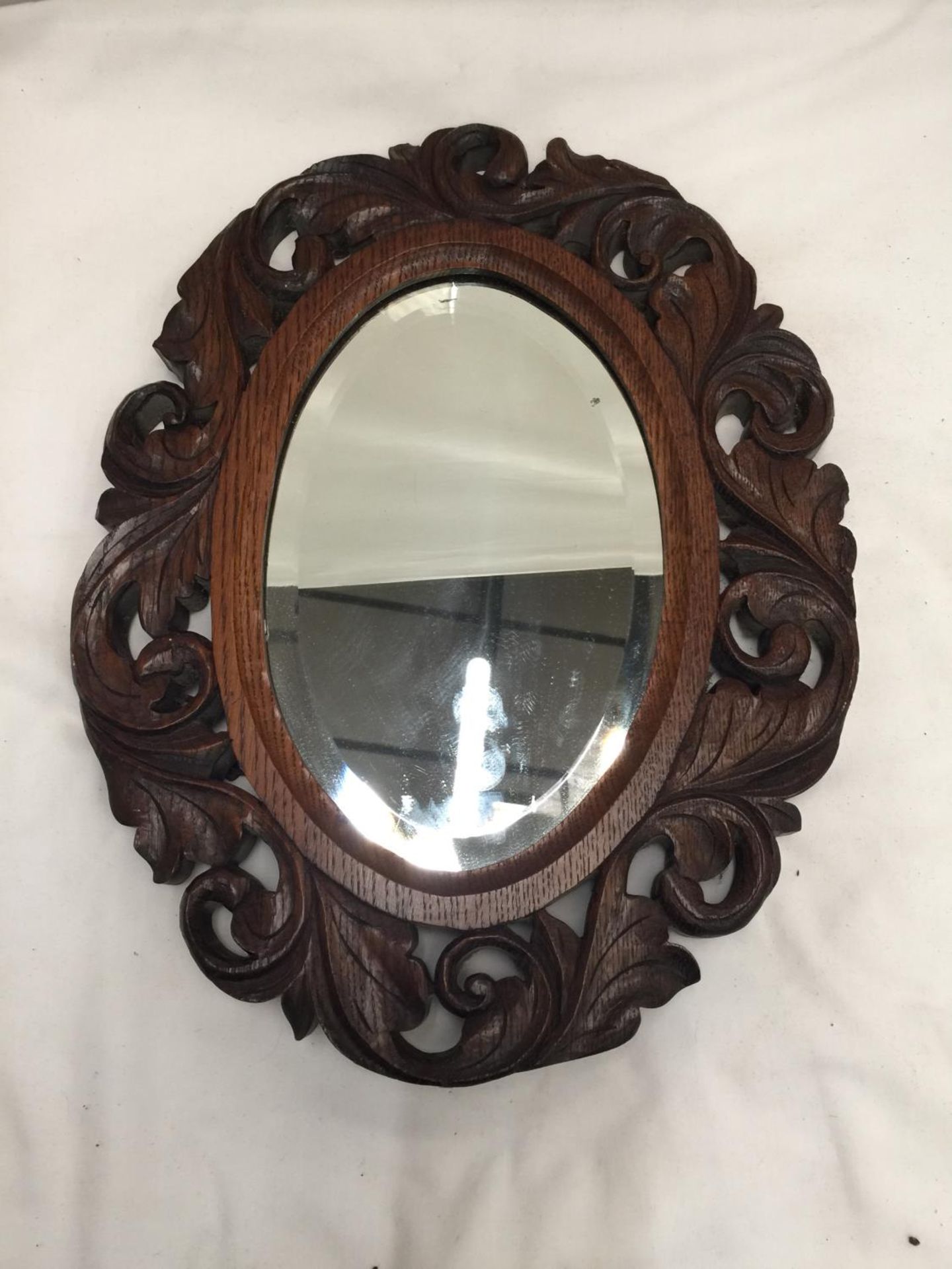AN CARVED OAK FRAMED OVAL MIRROR WITH BEVELLED GLASS 39CM X 30CM