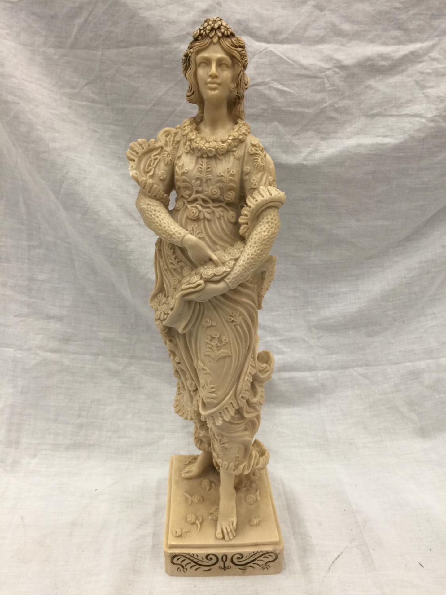 A CARVED RESIN FIGURE OF A GIRL WITH FLOWERS