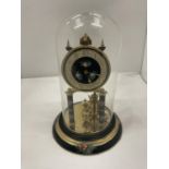 A BRASS AND CERAMIC ANNIVERSARY CLOCK WITH FLORAL DECORATION TO THE BASE AND FACE IN A GLASS DOME,